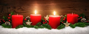 Low-key studio shot of elegant advent decoration with fir branches on snow and tow burning red candles, dark wood background