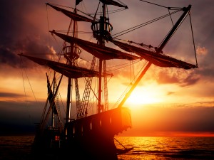 Old ancient pirate ship on peaceful ocean at sunset. Calm waves reflection, sun setting.