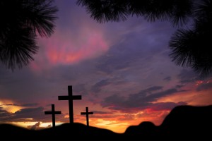 Easter.  The crucifixion with three crosses in silhouette stand silently on a landscape scene with a dramatic sky in purple hues.  Christianity, religious themes. Copyspace.