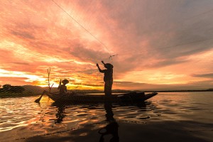 Silhouette Fisherman Fishing by using Net on the boat in morning in Thailand, Nature and culture concept